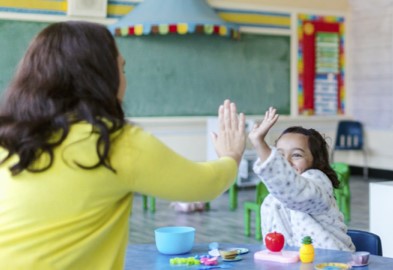 A child at table high fiving her teacher